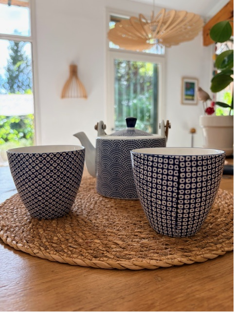 Théière et deux bols à motifs sur un set tressé, ambiance maison lumineuse